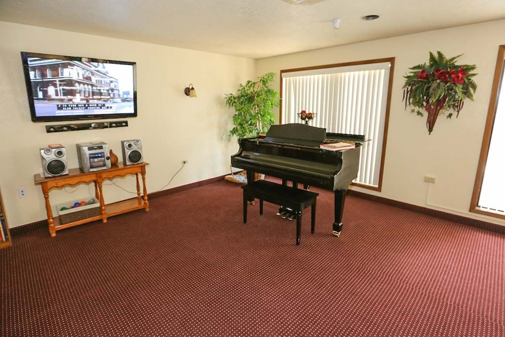 A cozy living room featuring a piano, TV, and house plants.