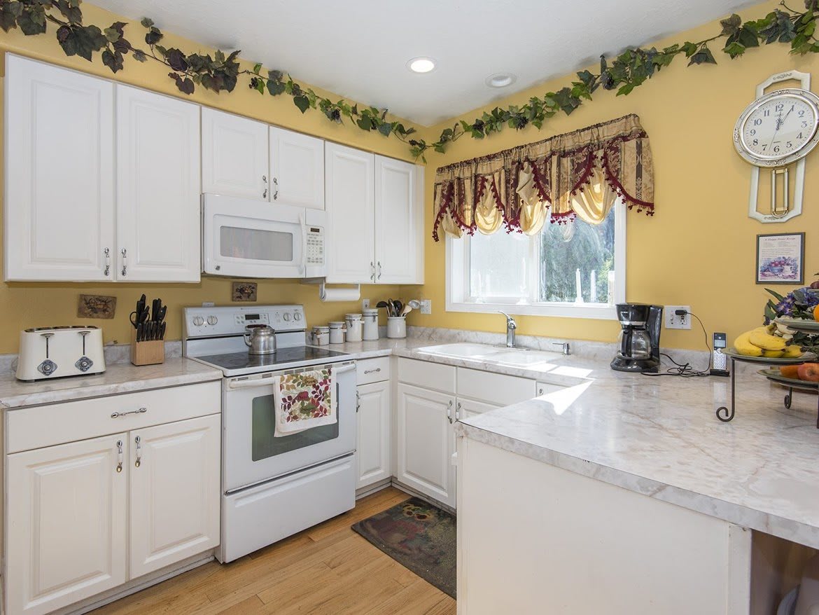 A cozy kitchen with white cabinets, yellow walls, and decorative vine accents.