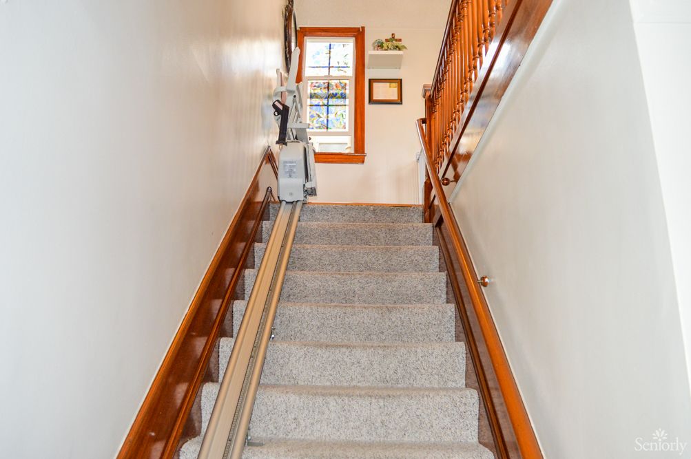 A staircase equipped with a stair lift for accessibility, featuring carpeted steps and wooden handrails.
