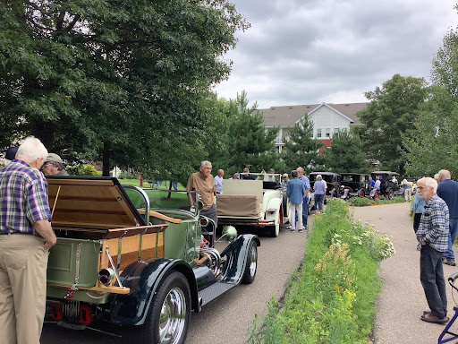 A gathering of vintage car enthusiasts showcasing their classic automobiles on a cloudy day.