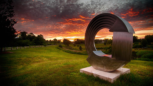 A stunning metal sculpture set against a vibrant sunset, creating a beautiful contrast with the lush green landscape.