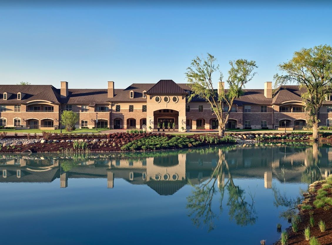 A grand building with elegant architecture is beautifully reflected in a calm lake, surrounded by lush greenery.