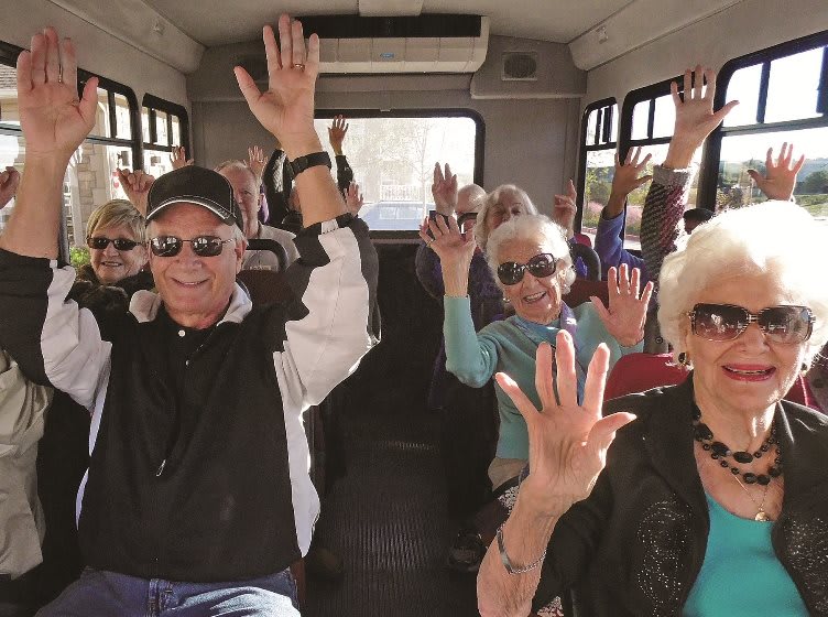 A group of seniors enjoying a lively bus ride, raising their hands in excitement.