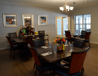 A well-lit dining room with neatly arranged tables and chairs, decorated with flowers and artwork.