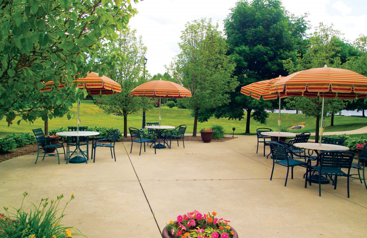 A tranquil outdoor patio with tables, chairs, and umbrellas surrounded by lush greenery.