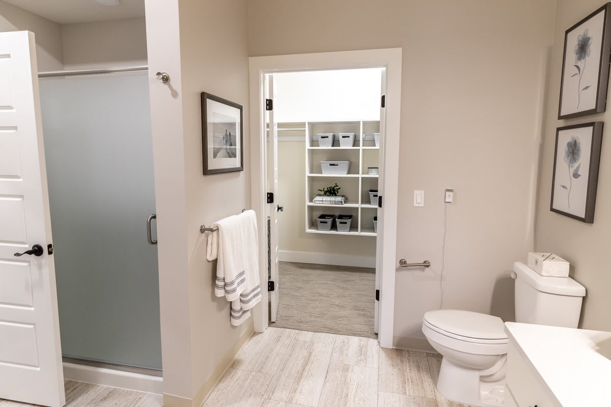 A modern bathroom with a shower, toilet, and open doorway showing shelves in the background.