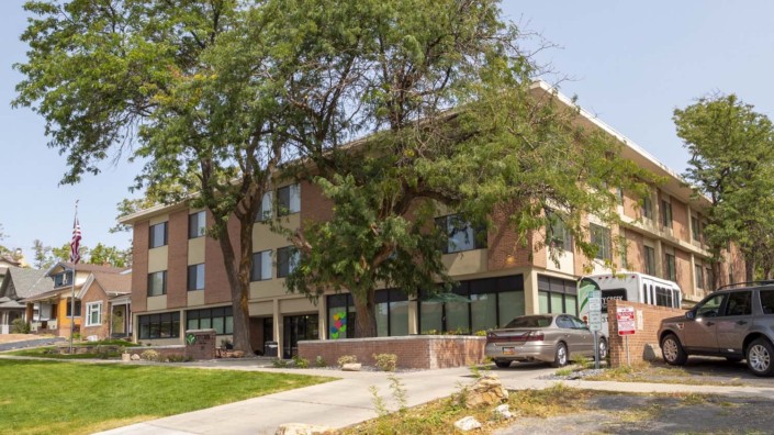 A three-story brick building with trees and a parked car in front.
