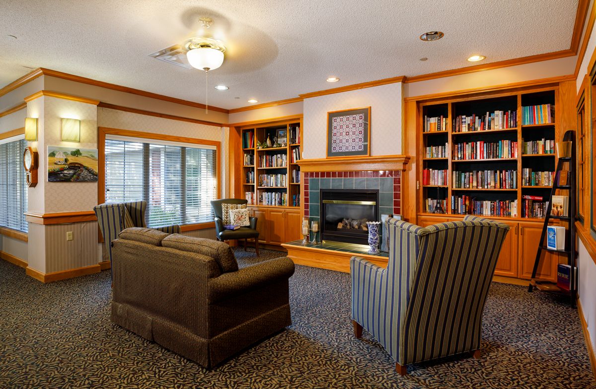 A cozy living room with a library and fireplace, featuring comfortable seating and bookshelves.