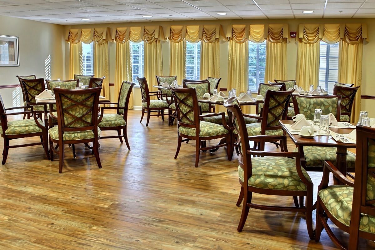 An elegant dining room with neatly arranged tables and chairs, featuring wooden flooring and decorative curtains.