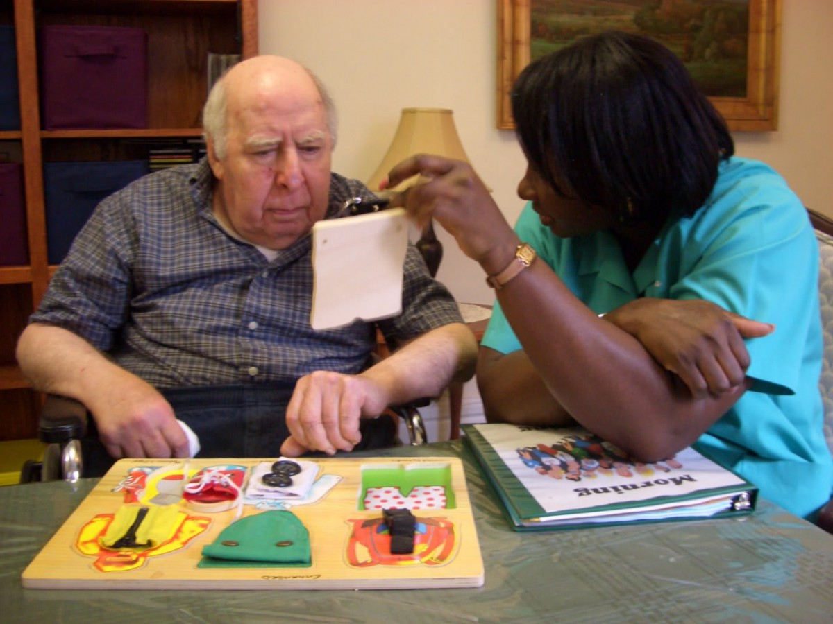 A caregiver assisting an elderly man with an activity at a nursing home.