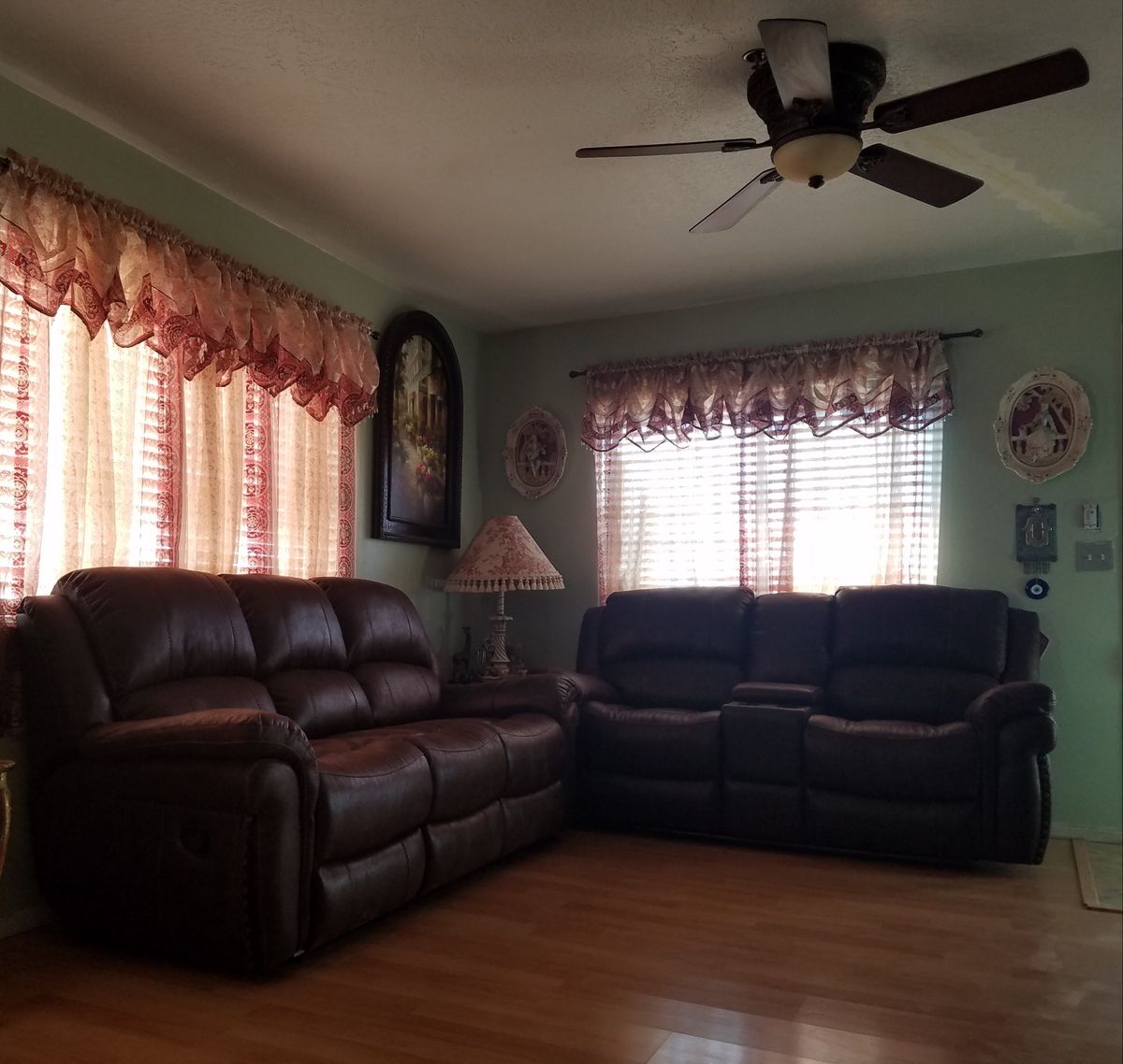 A cozy living room with leather sofas, a ceiling fan, and windows adorned with curtains.