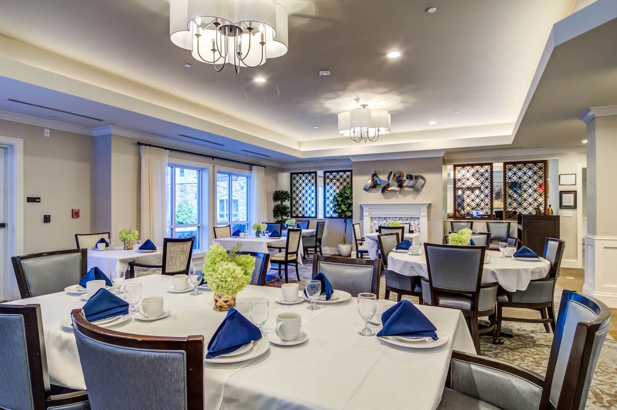 An elegantly designed dining area with neatly arranged tables and chairs, adorned with chandeliers and blue napkins.