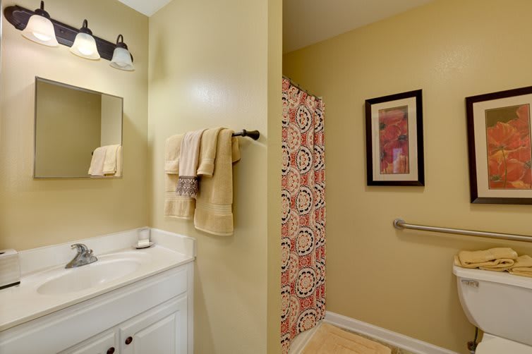 A well-lit bathroom featuring a shower with a patterned curtain, a sink with towels, and modern wall art.