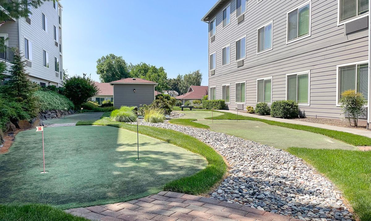 A well-maintained garden area with a putting green next to an apartment building.