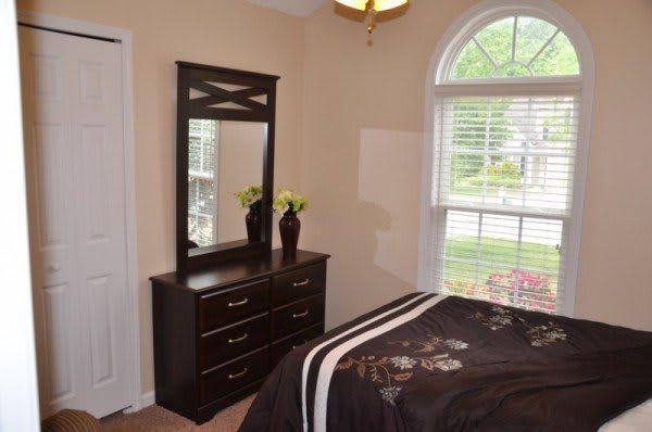 A cozy bedroom with a dark dresser, mirror, and large window.