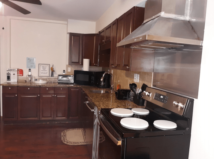 A modern kitchen with dark wooden cabinets, stainless steel appliances, and a stovetop with white dishes.