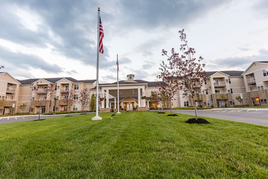 A large building with flags at the entrance, surrounded by a well-maintained lawn and trees under a cloudy sky.
