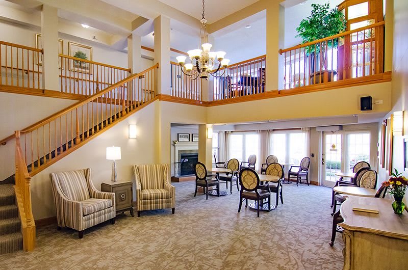 A spacious and elegantly designed living room with a staircase, dining tables, and comfortable seating.