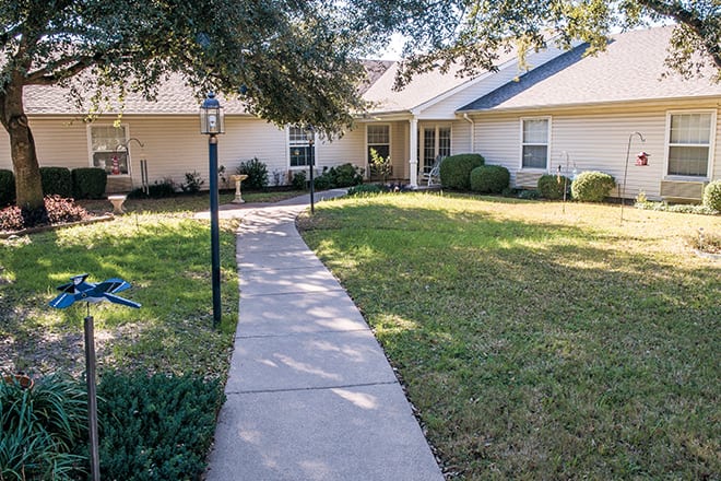 A pathway leading to a residential house surrounded by a well-maintained lawn and trees.