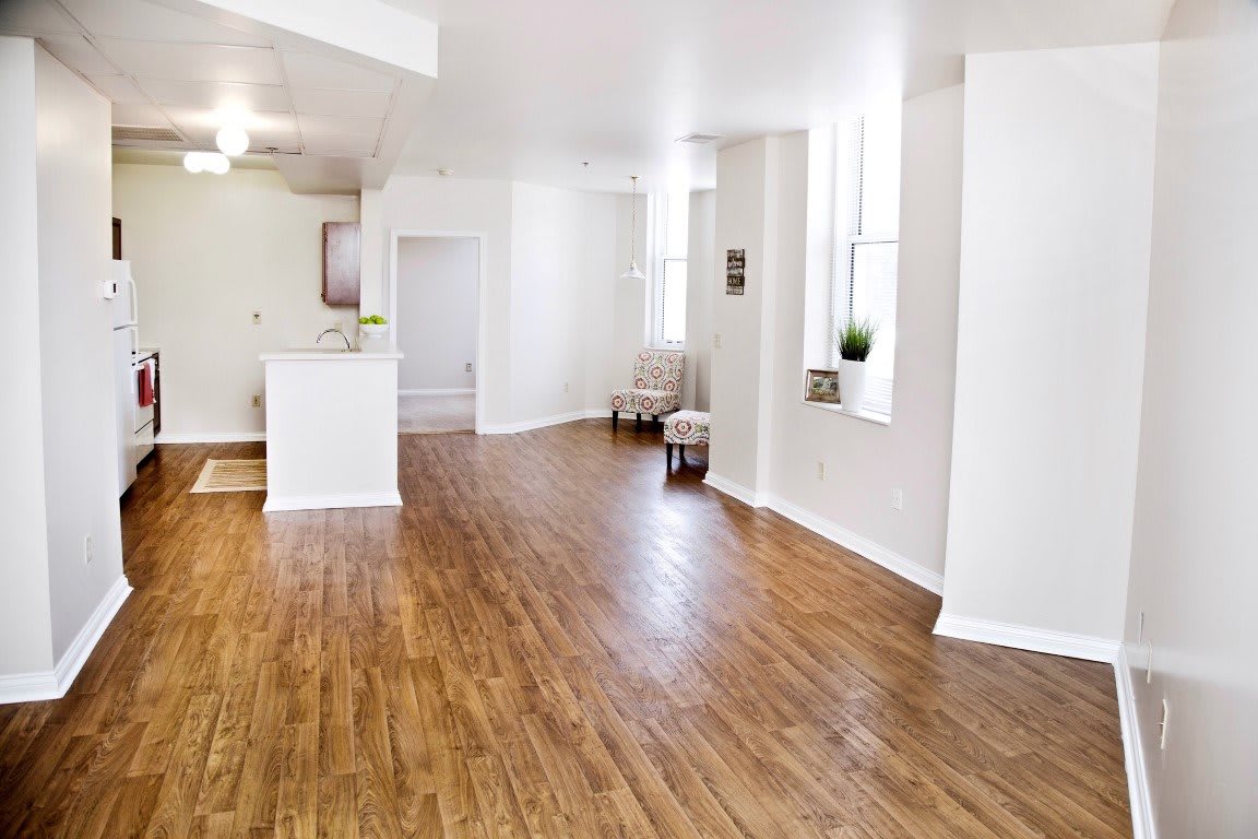 A spacious and minimalist open-plan living area with wood flooring and abundant natural light.