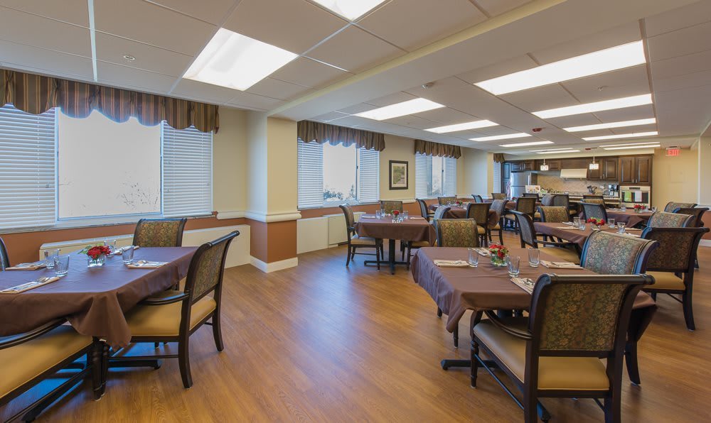 A spacious dining area with neatly arranged tables and chairs, featuring warm lighting and a wooden floor.