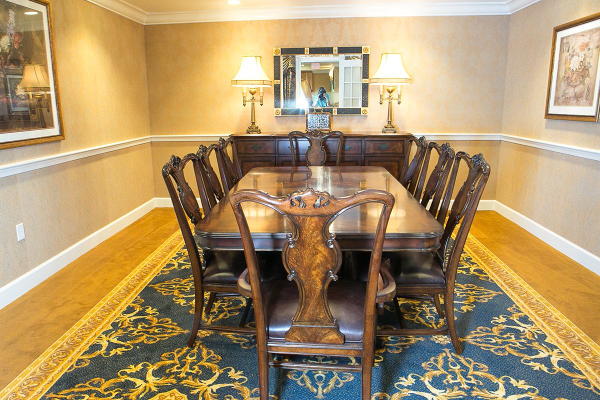 A traditional dining room with a wooden table and matching chairs, featuring two lamps and a decorative mirror on the wall.