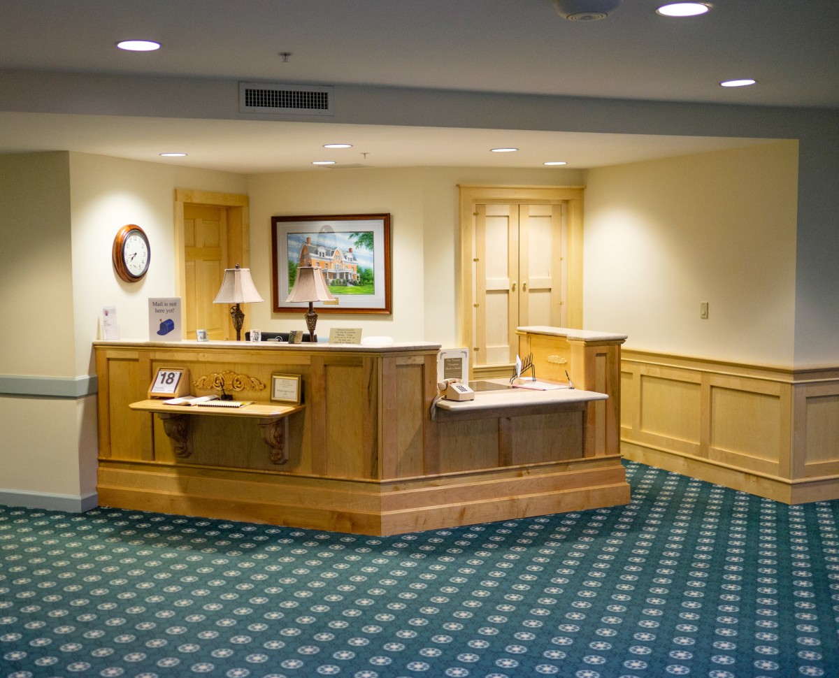 A well-lit office lobby featuring a wooden reception desk with artwork and a lamp.