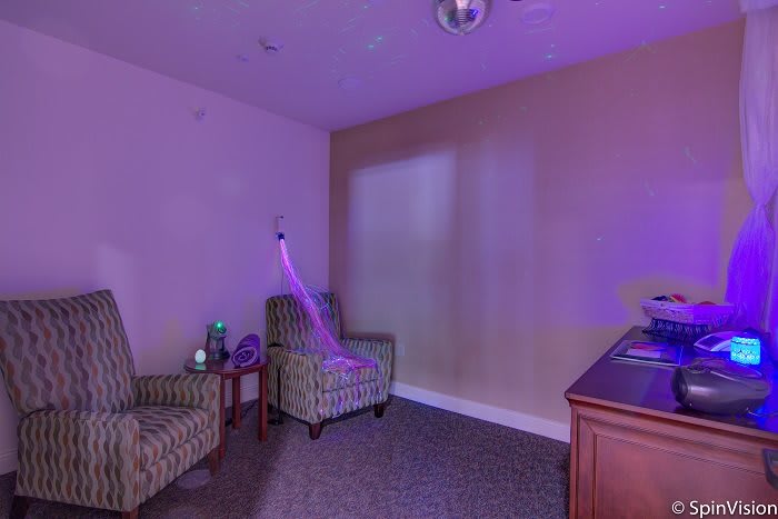 A cozy room with purple lighting featuring two chairs and a small table.