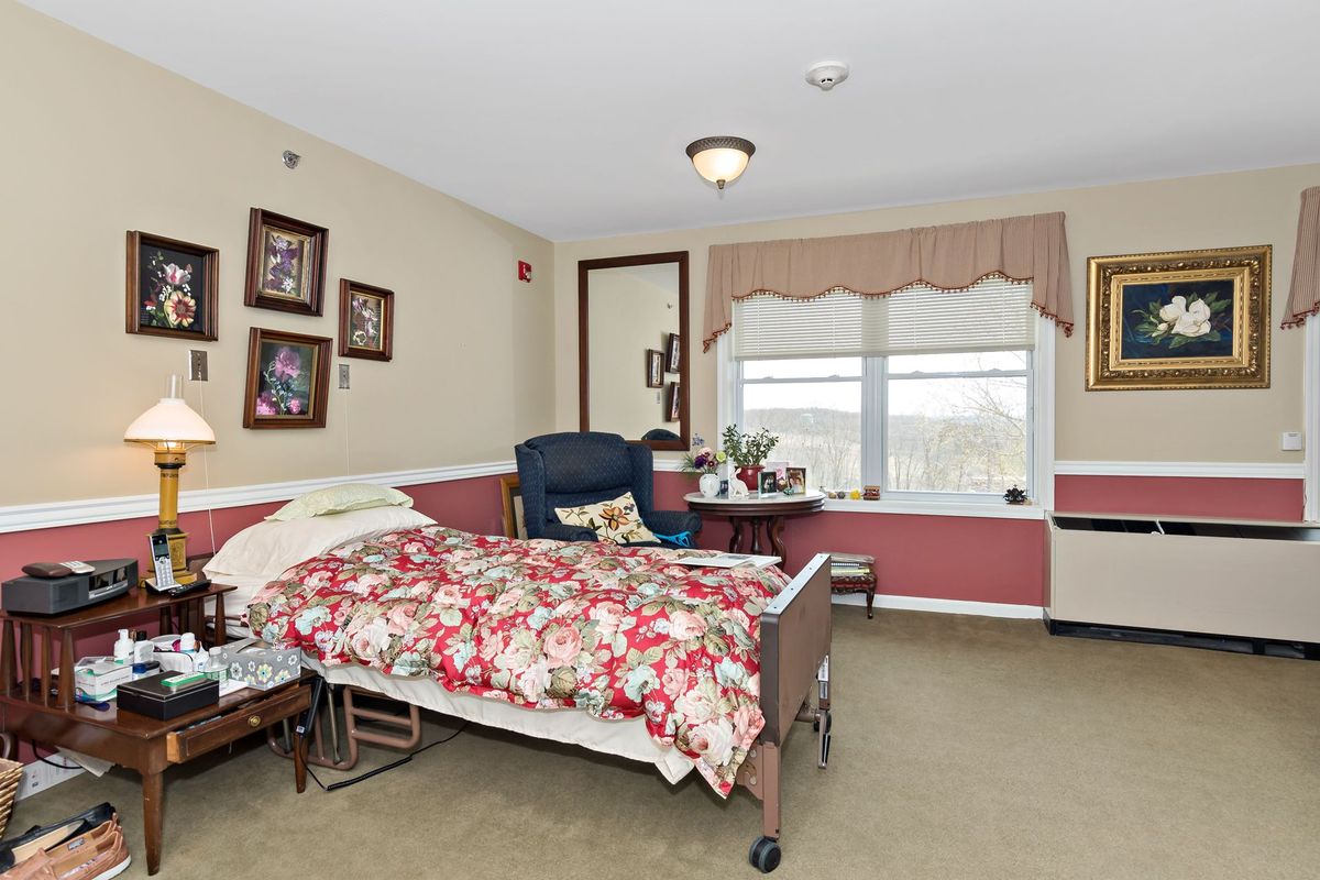 A cozy and well-decorated bedroom with a hospital bed, featuring framed pictures on the wall and a large window overlooking the view.