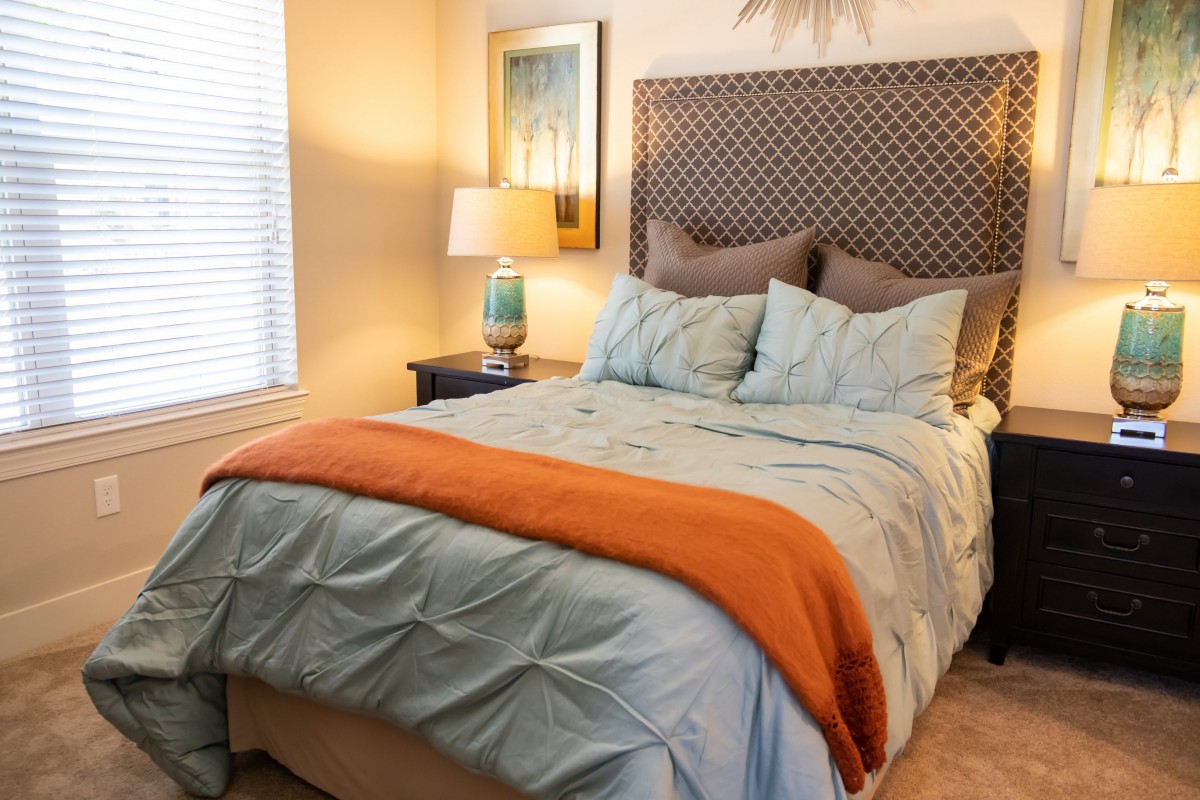 A cozy bedroom with a neatly made bed featuring blue and orange bedding, complemented by a bedside lamp and artwork on the wall.