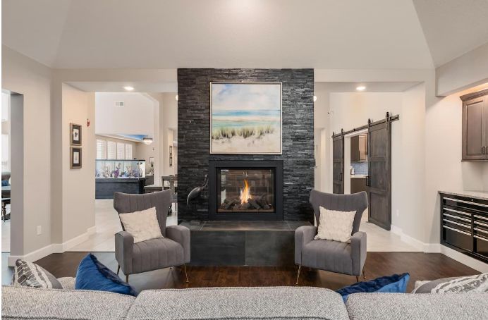 A modern living room with a central fireplace, flanked by two armchairs and decorated with a painting above.