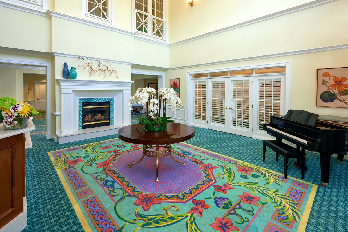 A well-decorated living room with a fireplace, piano, colorful rug, and elegant table centerpiece.
