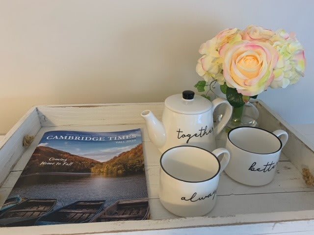 A cozy setup with a teapot, two mugs, a magazine, and flowers on a tray.