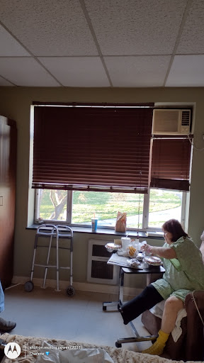A cozy room with blinds drawn over the window, featuring a person sitting at a table.