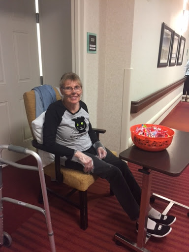 An elderly woman smiling while sitting in a chair in an assisted living facility.