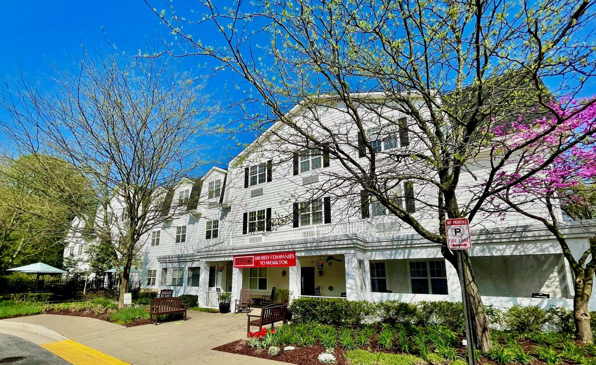 A three-story residential building with a red awning, surrounded by trees on a clear day.