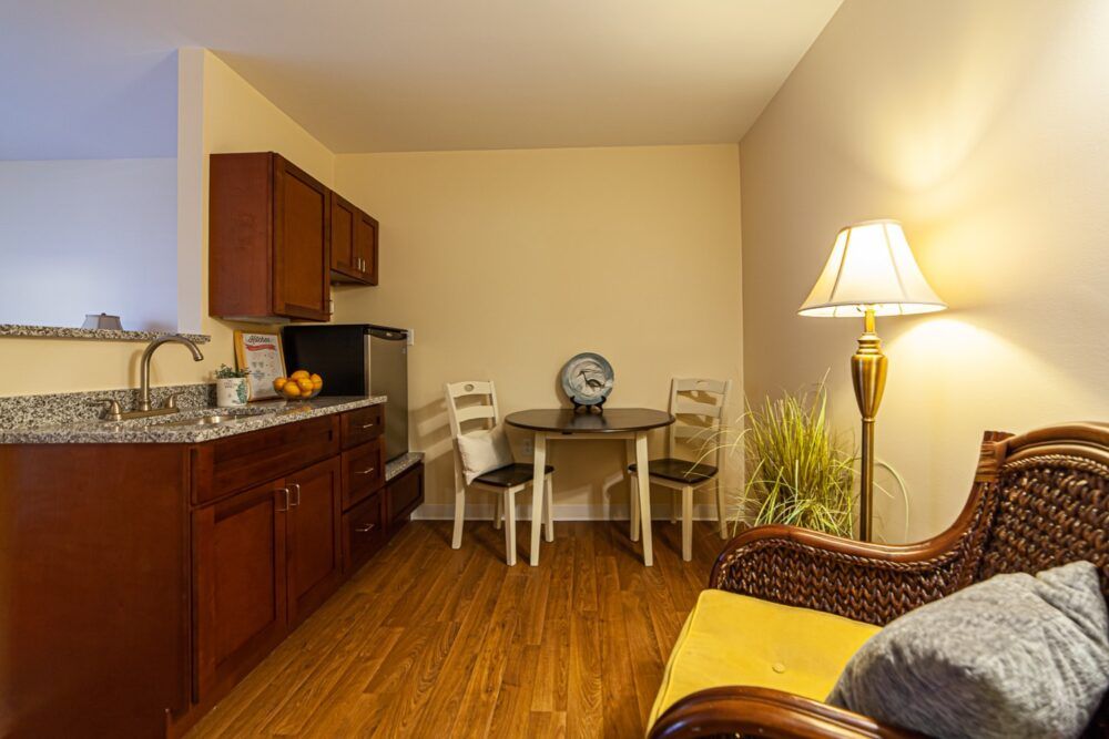 Cozy kitchen and dining area with wooden cabinets, a round table with chairs, a lamp, and small refrigerator.