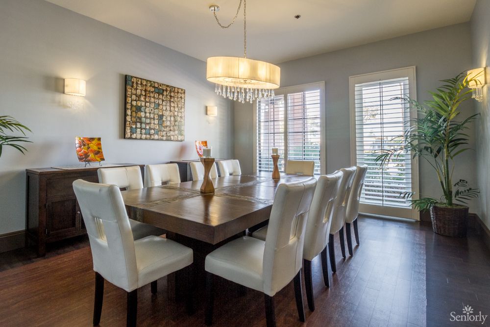 A modern dining room with a large table surrounded by white chairs and illuminated by a stylish chandelier.