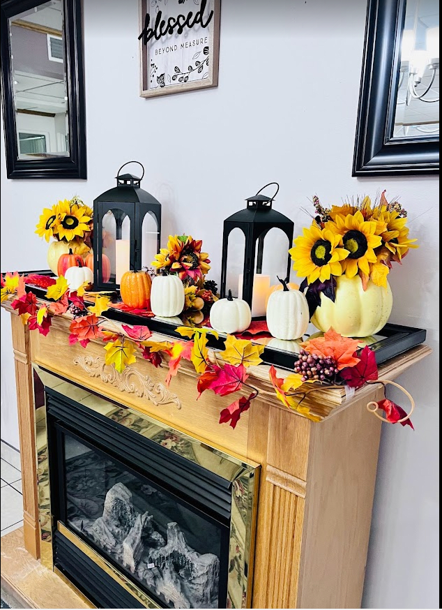 A cozy autumn-themed fireplace decoration with sunflowers, pumpkins, candles, and colorful leaves.