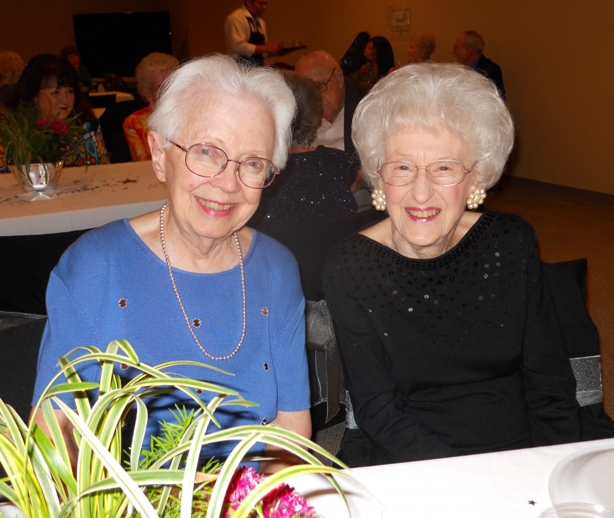 Two elderly women smiling at an indoor event.