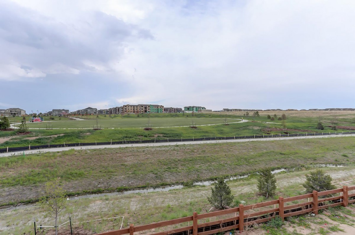A suburban landscape with a grassy field, cloudy sky, and distant houses.