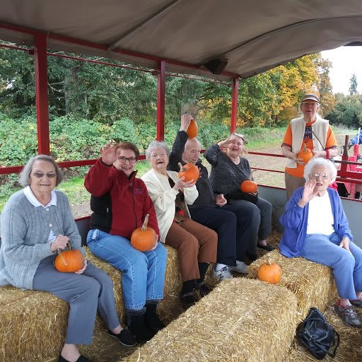 A group of people enjoying a hayride while holding pumpkins during an autumn outing.