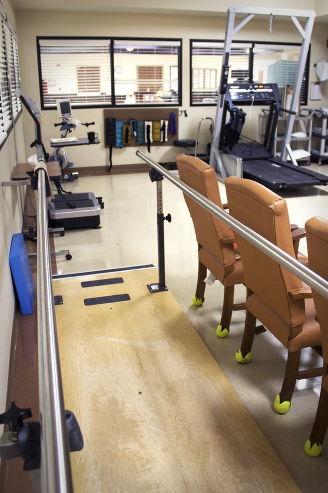 A rehabilitation room with parallel bars and various gym equipment.