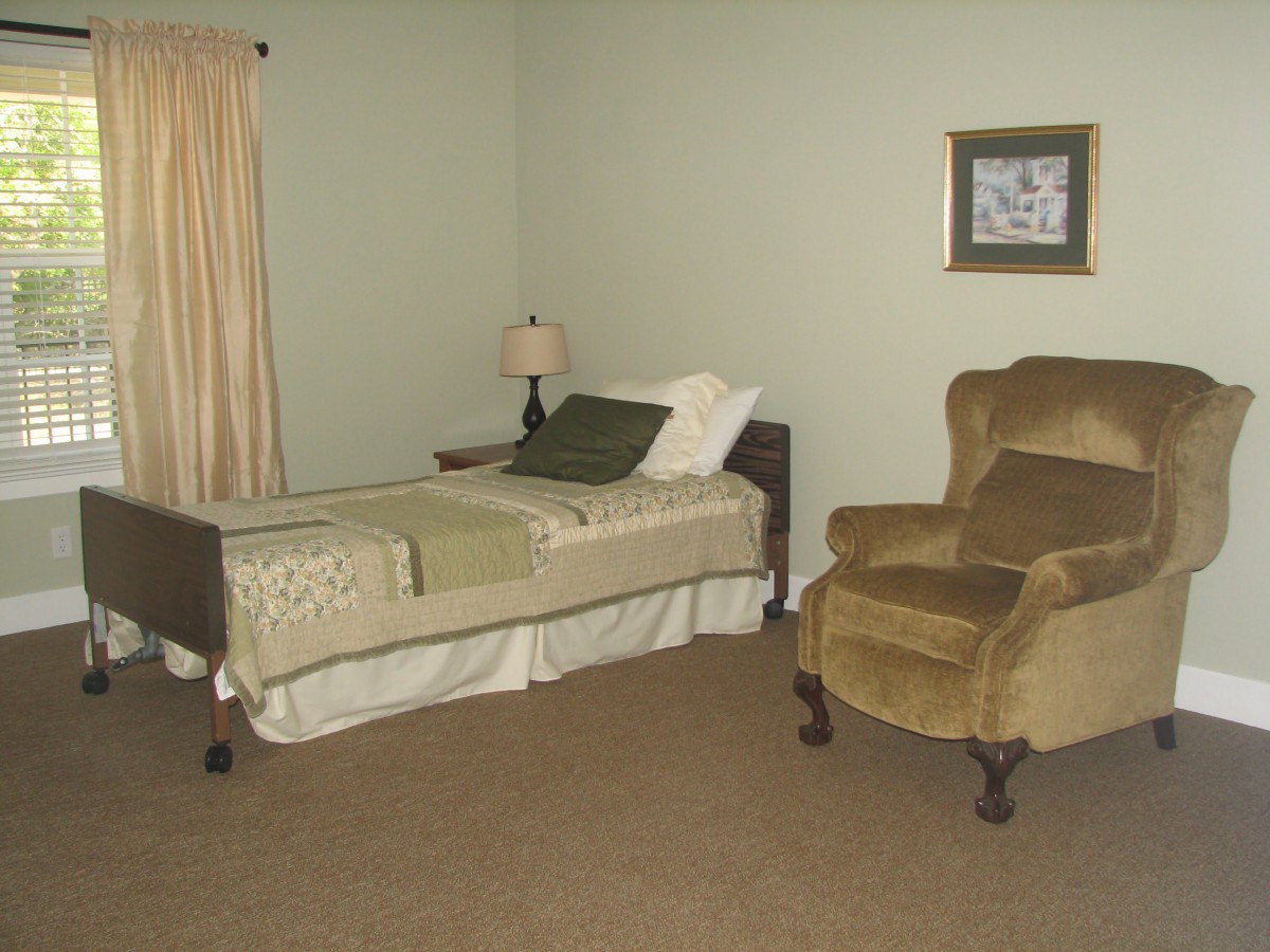 A simple bedroom with a single bed, an armchair, and a lamp beside the bed.