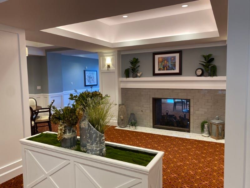 A cozy living room with a fireplace, decorated with plants and artwork.