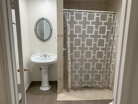 A neatly arranged bathroom with a pedestal sink, oval mirror, and patterned shower curtain.