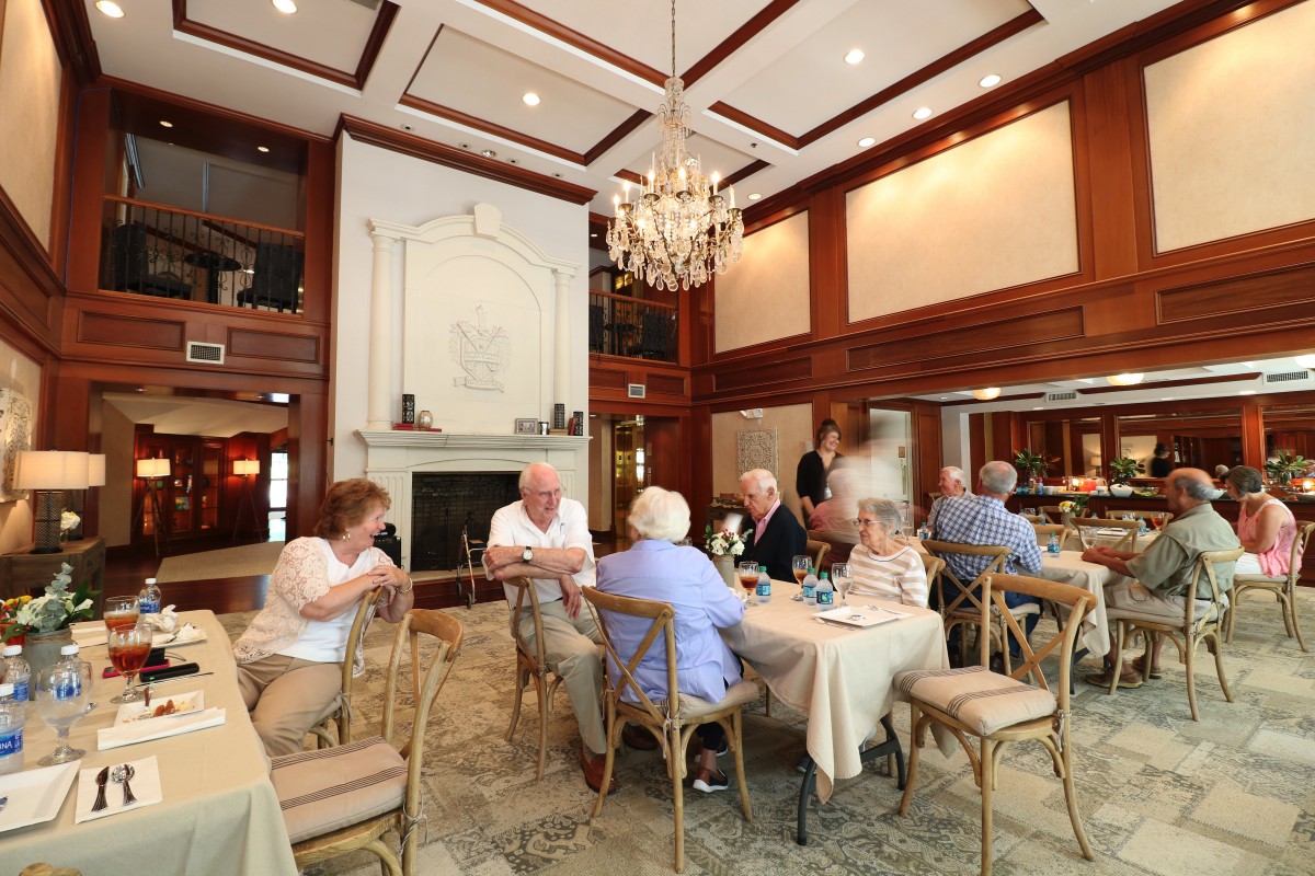 A group of people dining and socializing in an elegant restaurant interior with a chandelier.