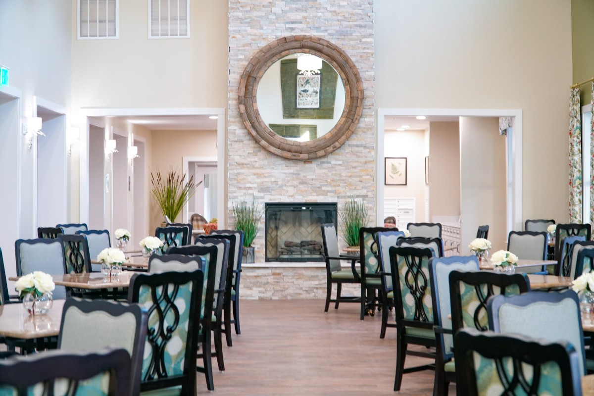 A modern dining room with elegantly set tables, a central fireplace, and a large decorative mirror.
