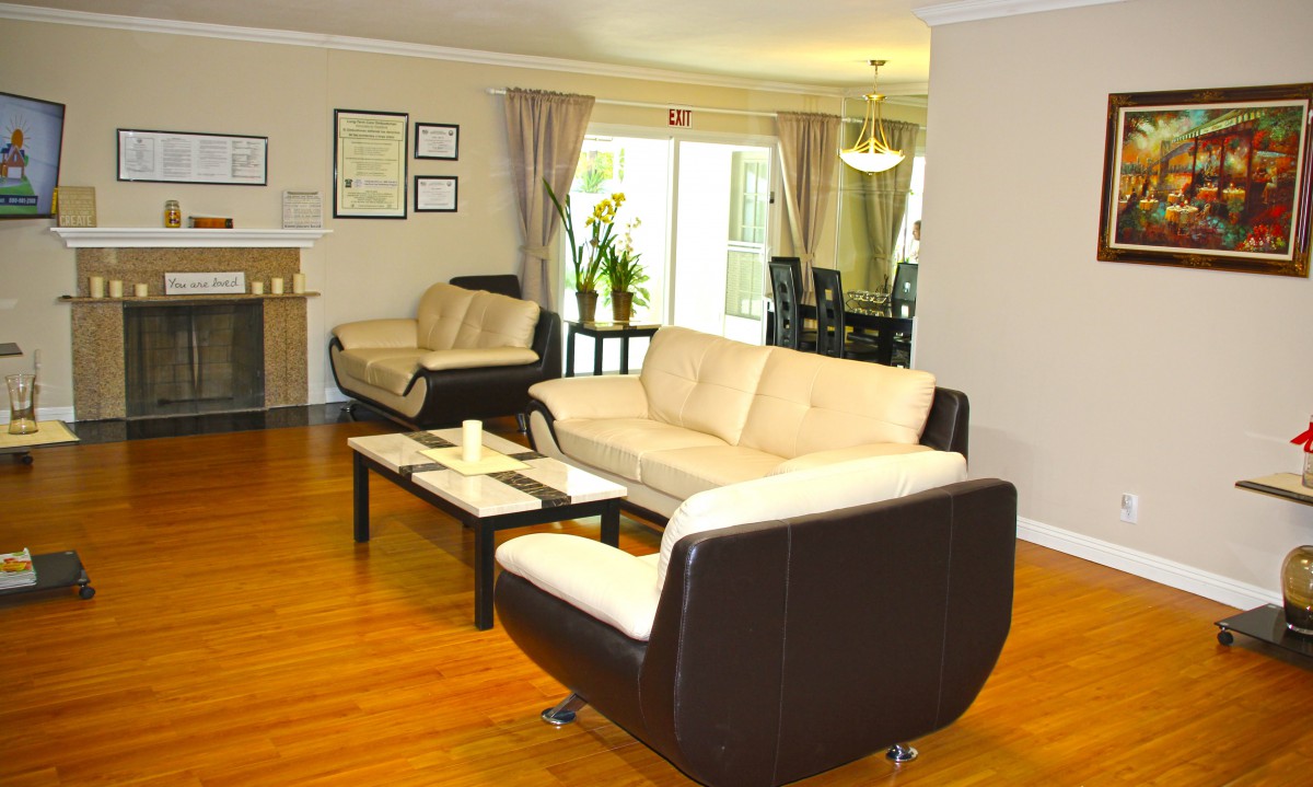 A modern living room featuring comfortable sofas, a coffee table, and a view into the dining area with flowing curtains.