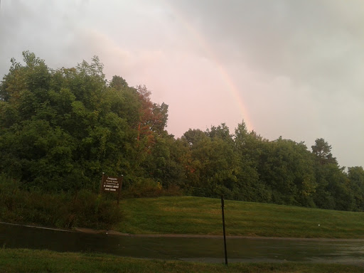 A subtle rainbow appears amidst the stormy clouds and lush greenery.